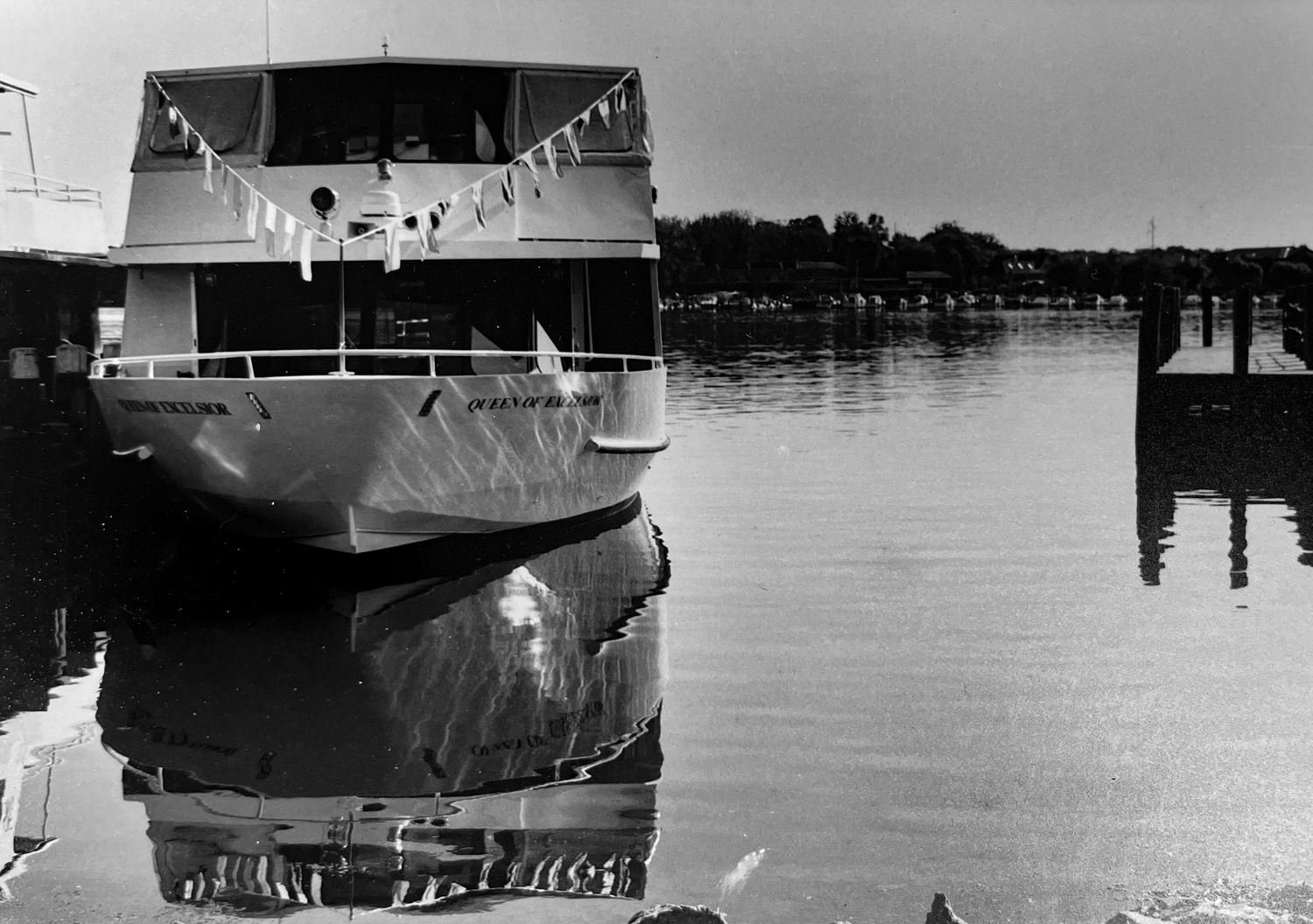 Black-and-white film photograph of a large boat on a lakefront dock