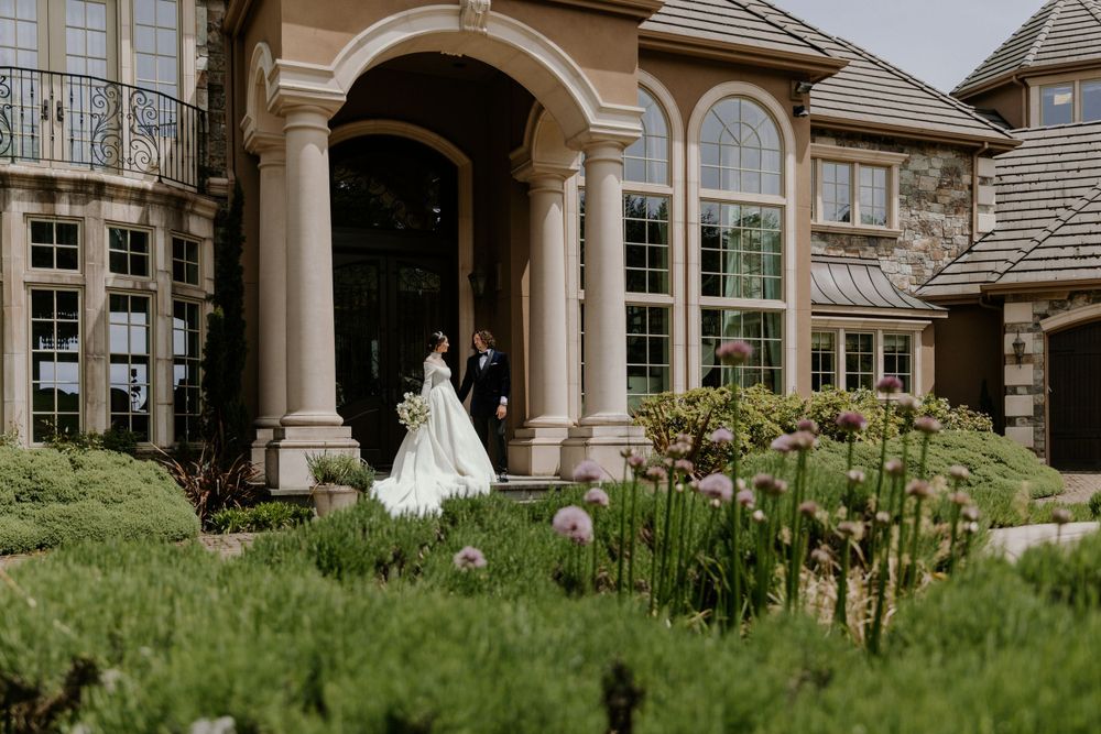 Wedding couple stands under an arched entrance of a luxurious stone mansion.