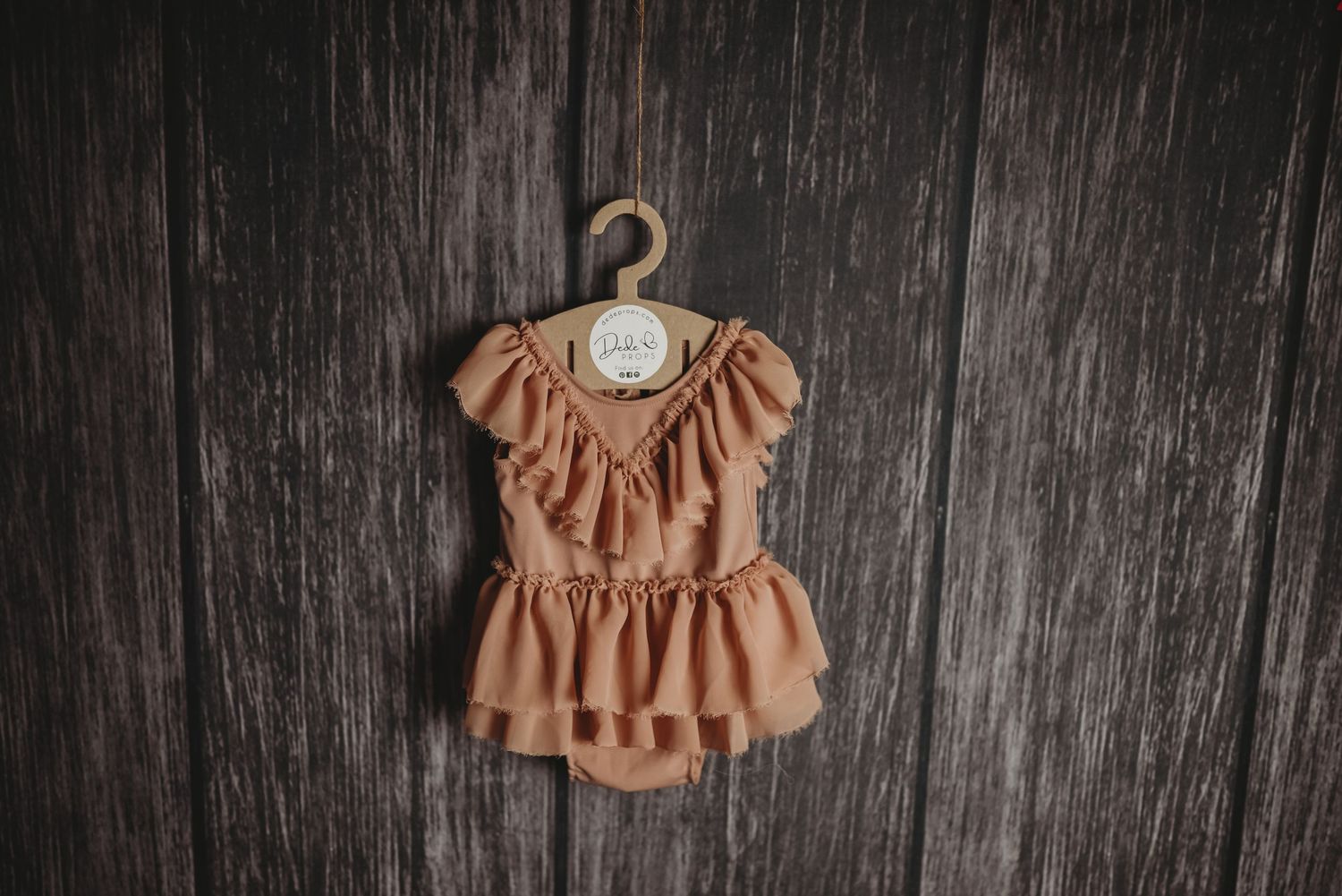 Peach-colored ruffled baby bodysuit displayed on dark wooden surface.