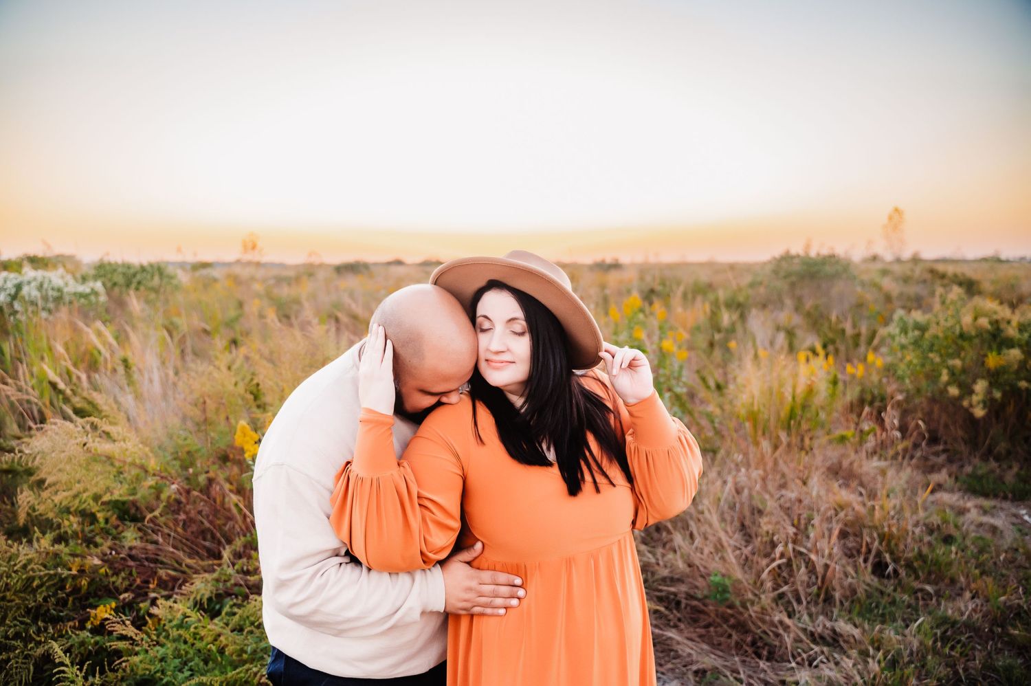 man kissing woman shoulder while she's holding brim of hat in Staten Island NY