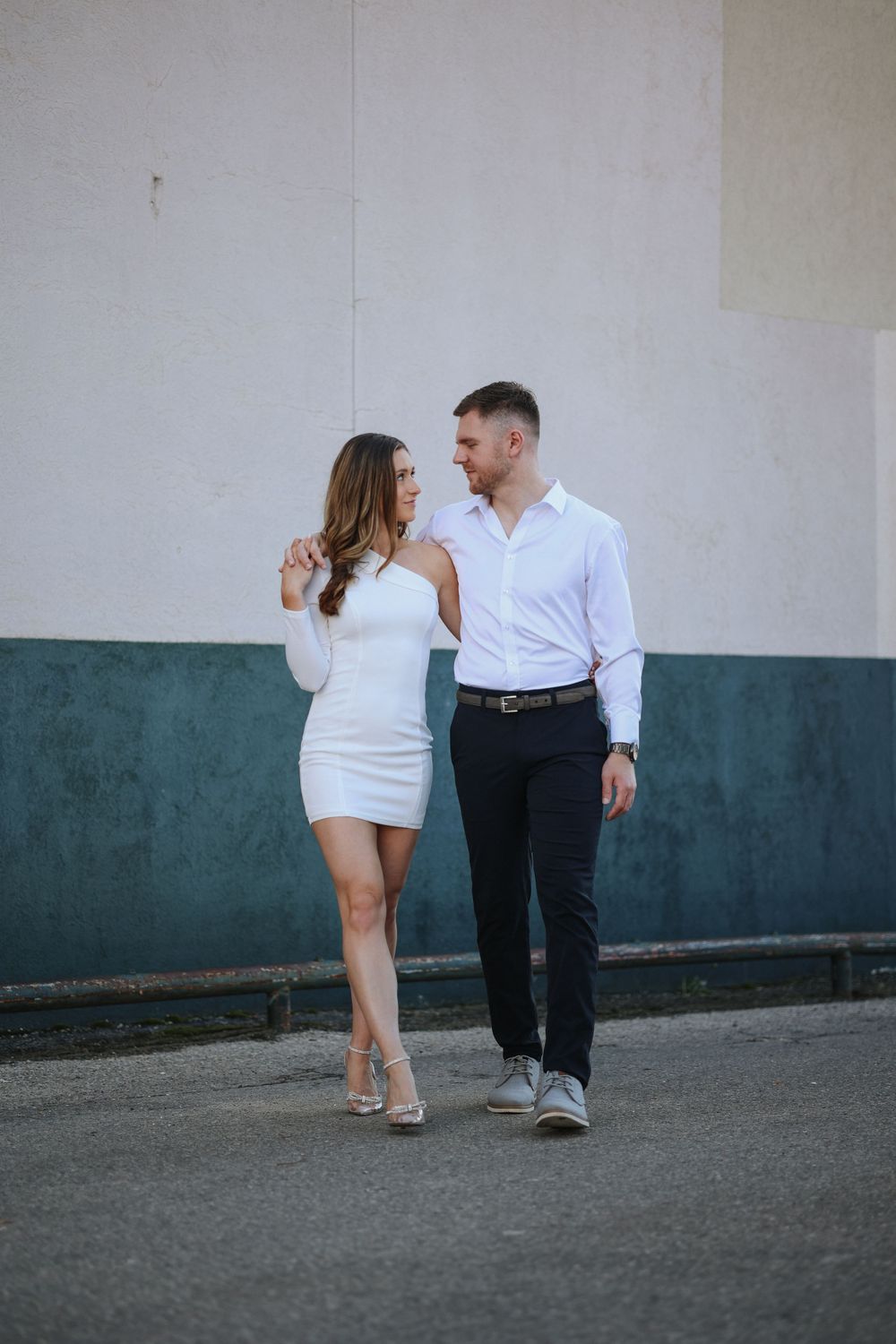 A couple in coordinated white outfits walking together along a wall with two-toned paint.