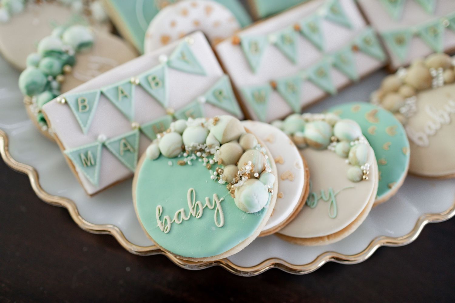 Close-up of mint green and white decorated sugar cookies with 'baby' text and bunting designs.
