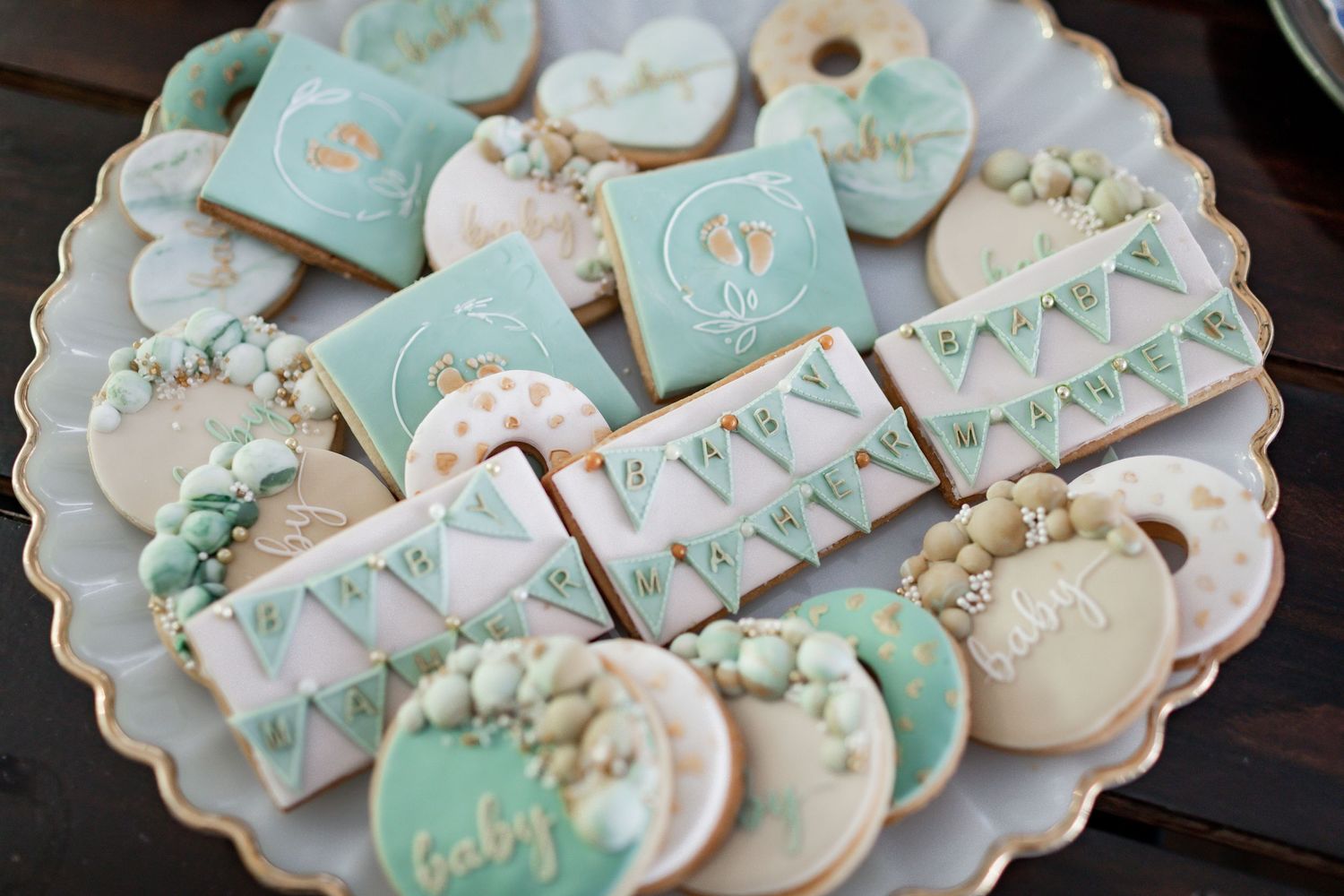 Beautifully decorated baby shower cookies in mint green and white with delicate floral details on a scalloped plate.