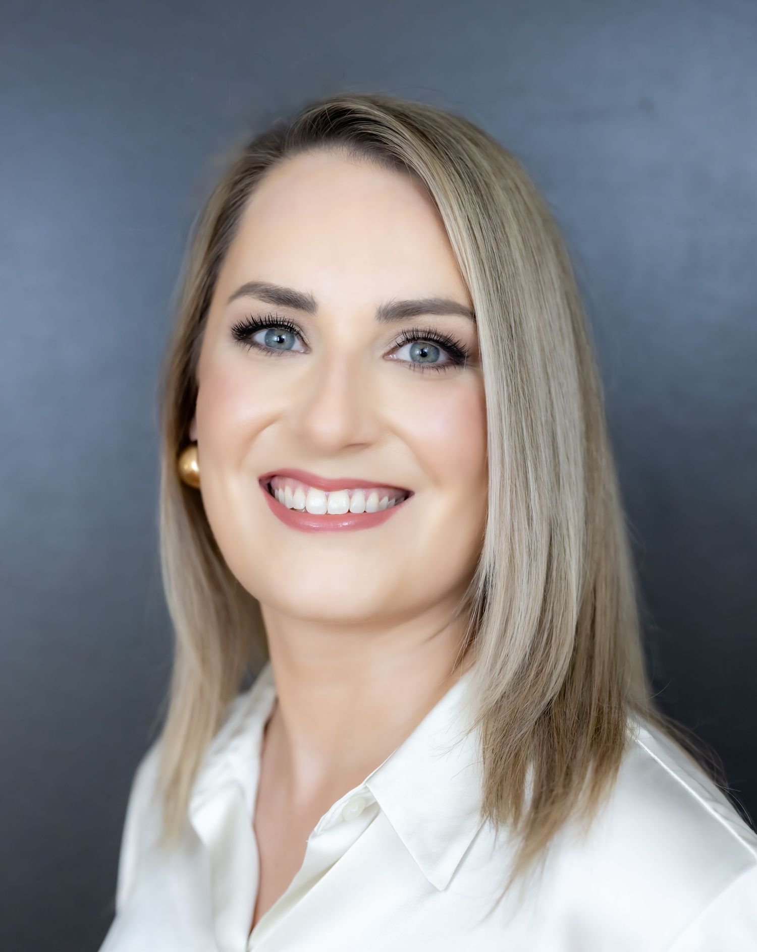 Professional headshot of person with blonde hair wearing white blouse against dark background.