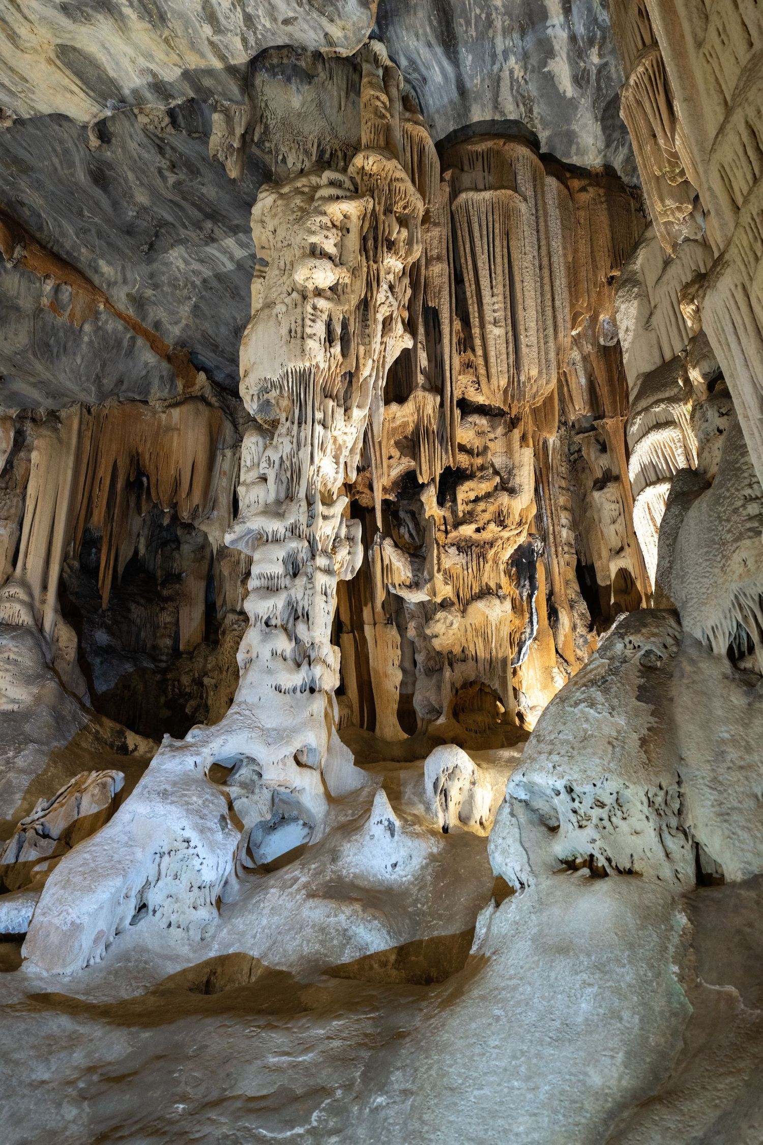 Ancient cave interior showing impressive stalactites and stalagmites lit by artificial lights.