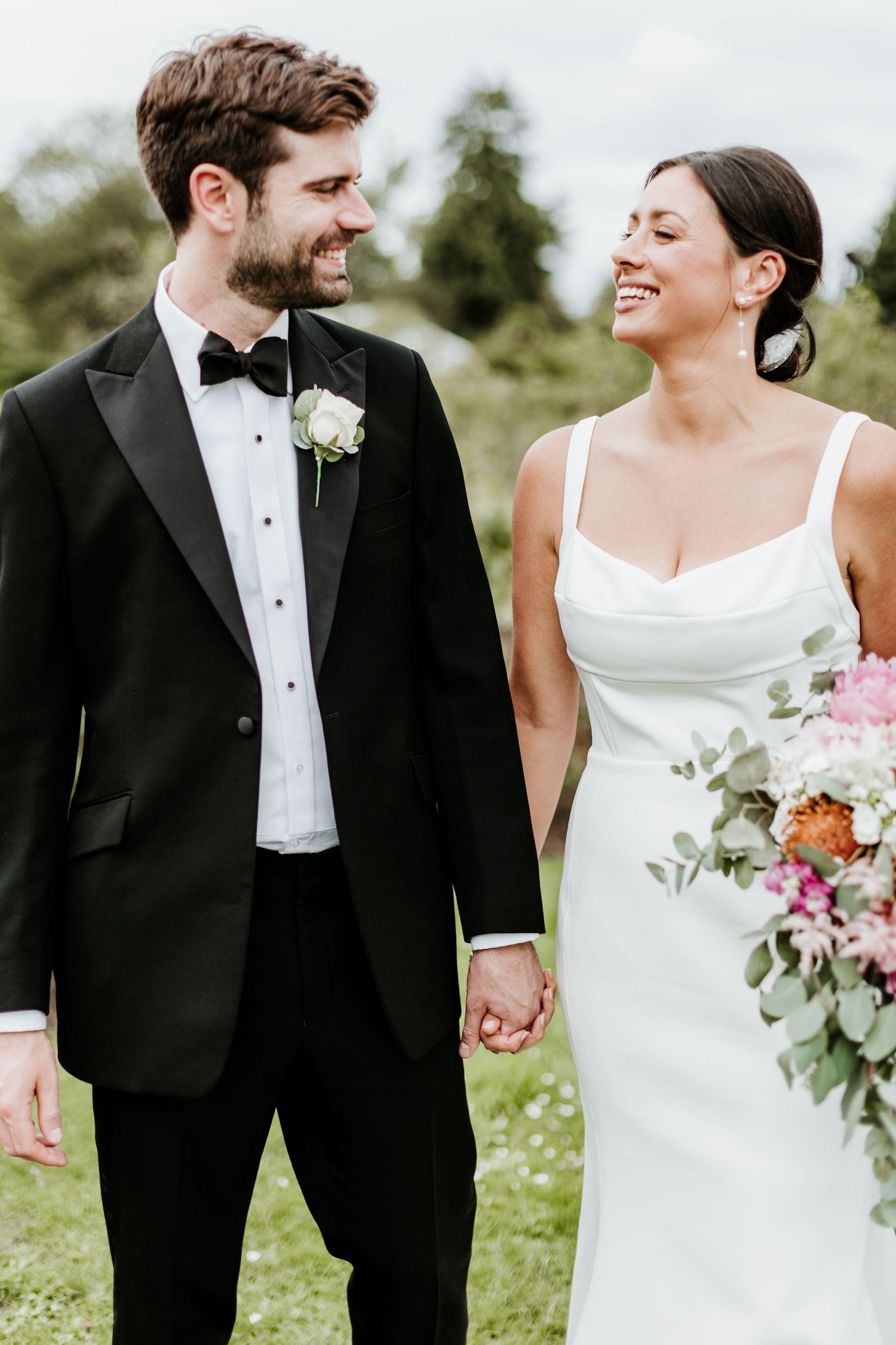 Newlywed couple sharing a joyful moment outdoors with floral bouquet.