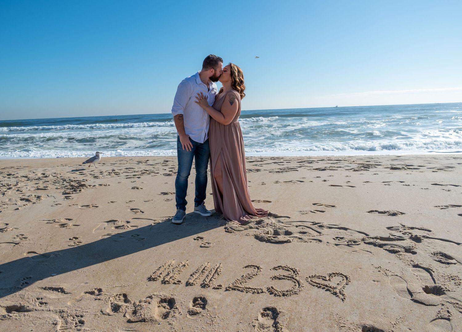 Beach engagement photoshoot with 2023 written in sand along the ocean shore.