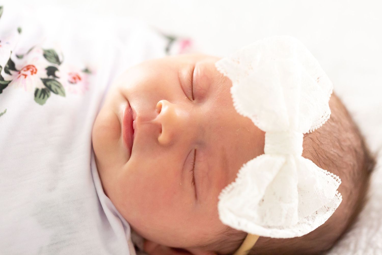 Peaceful sleeping newborn wearing delicate white bow headband on light fabric.