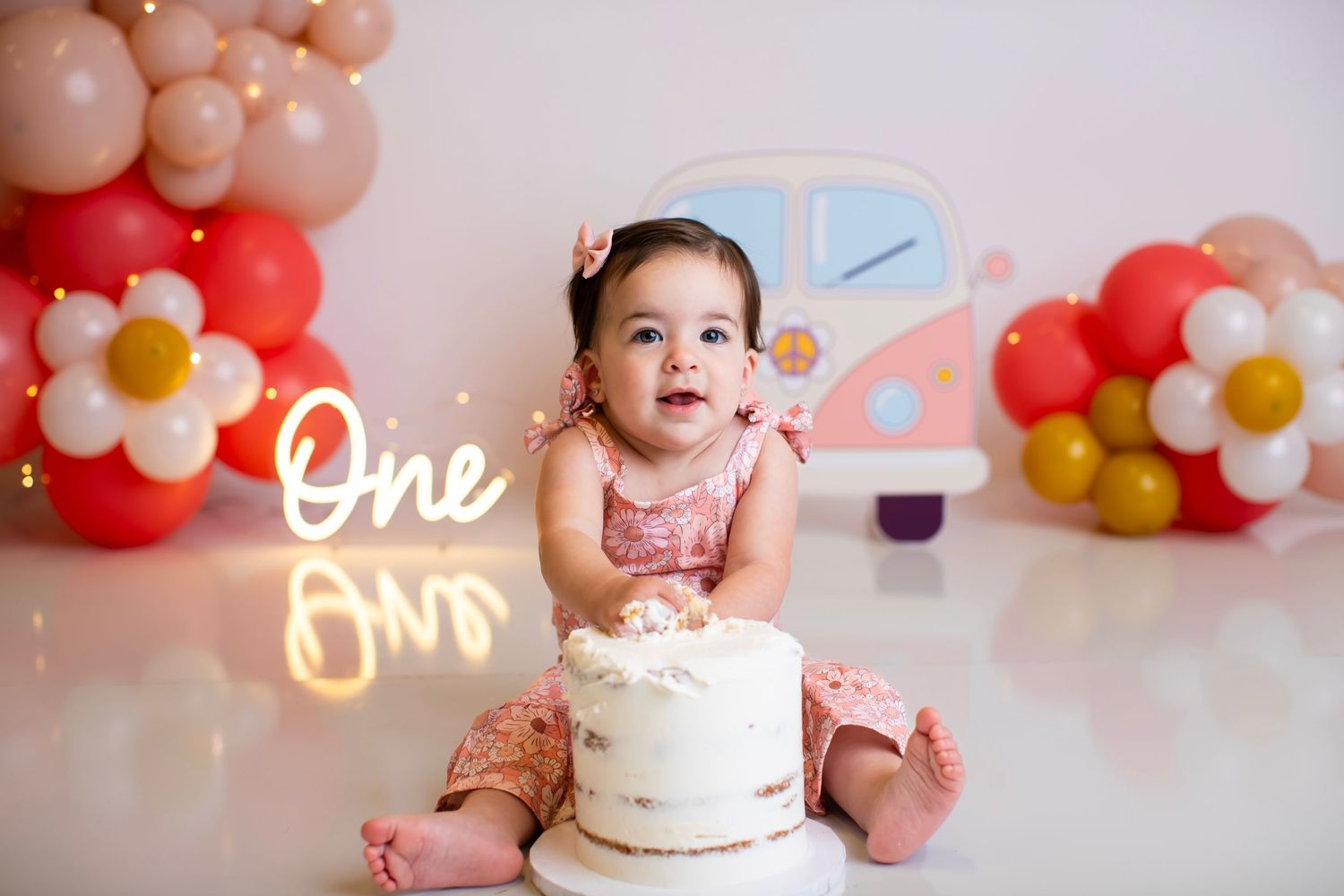 First birthday celebration setup with cake, balloons, and neon sign decorations.