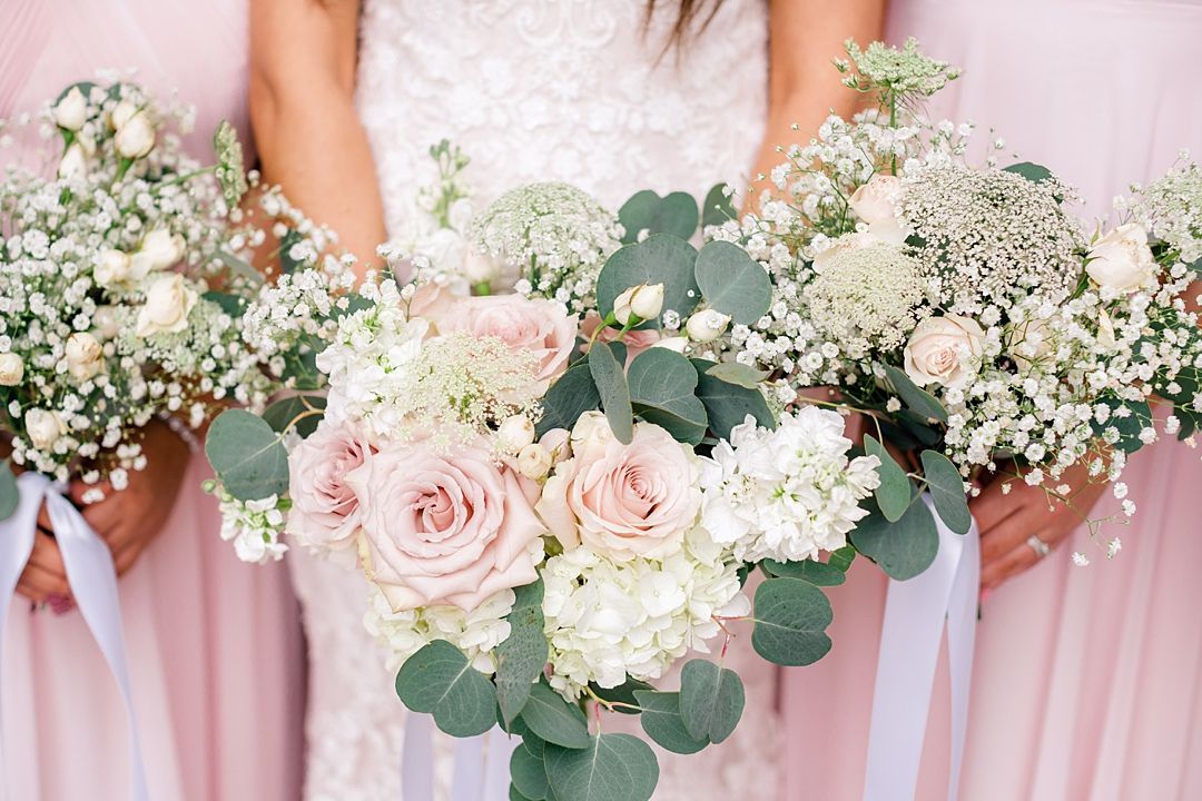 Elegant pink and white floral bouquets with roses, baby's breath and eucalyptus leaves held by bridesmaids in pink dresses.