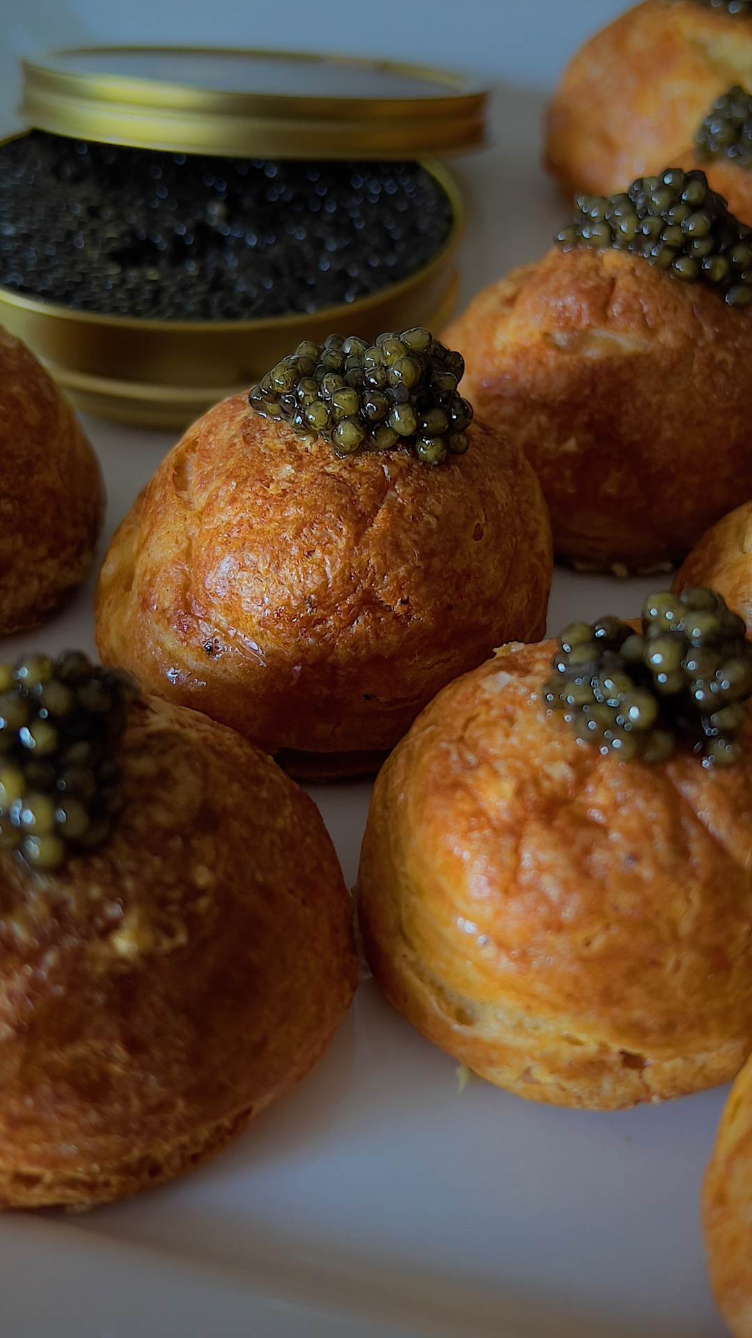 Golden pastry puffs topped with black caviar on a white plate.