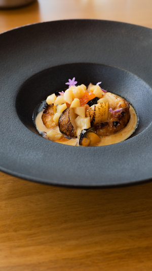 Expertly plated scallops and seafood in creamy sauce garnished with purple flowers.