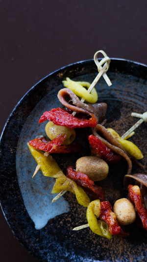 Colorful skewered appetizer with peppers, mushrooms and chorizo served on a dark plate.