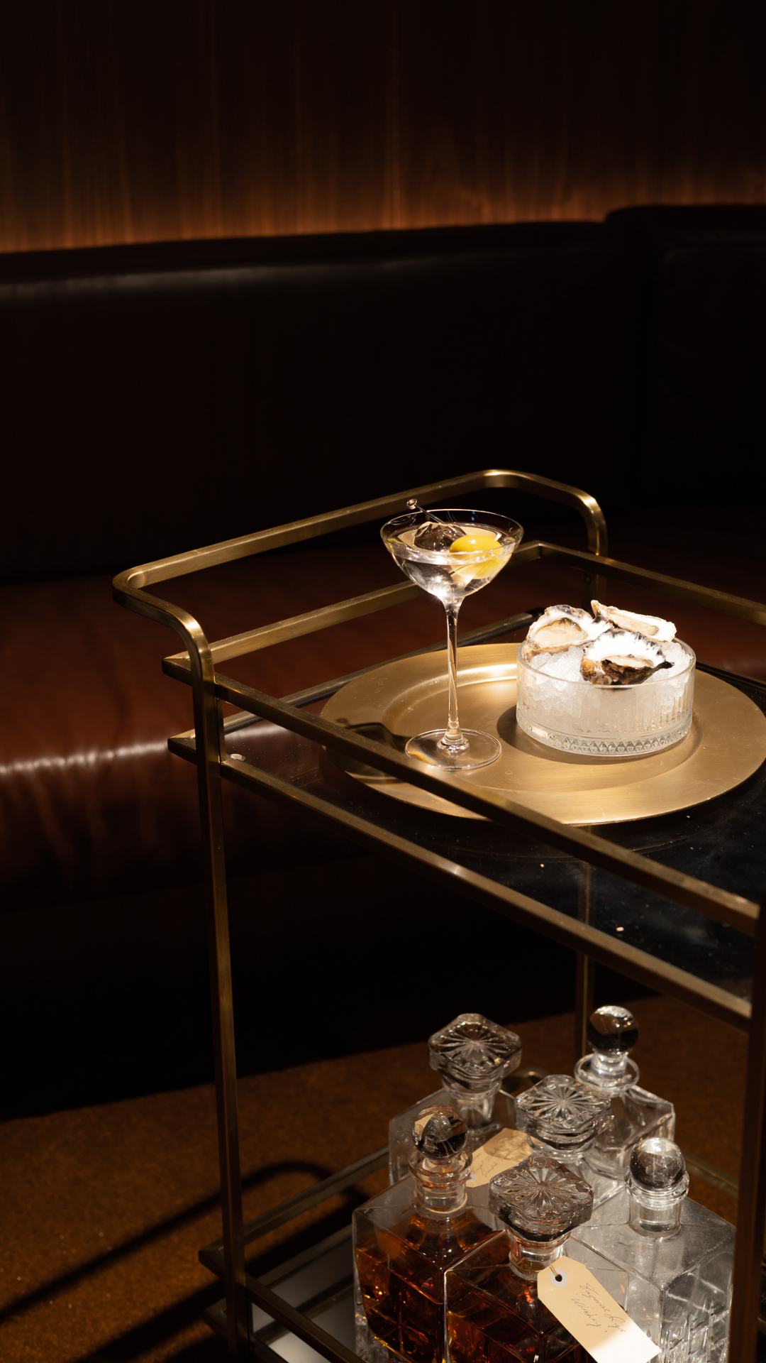 Luxurious bar cart setting with martini glass and dessert on leather seating backdrop.