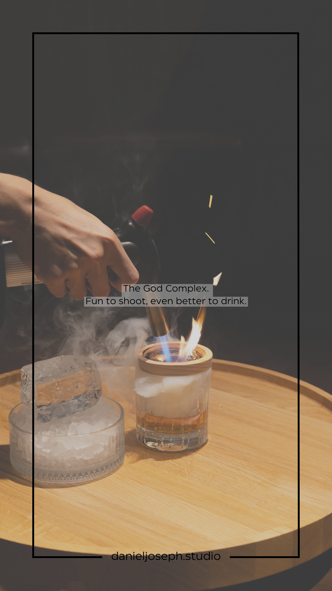 A hand torches a cocktail on a wooden serving tray creating dramatic flames and smoke effects.