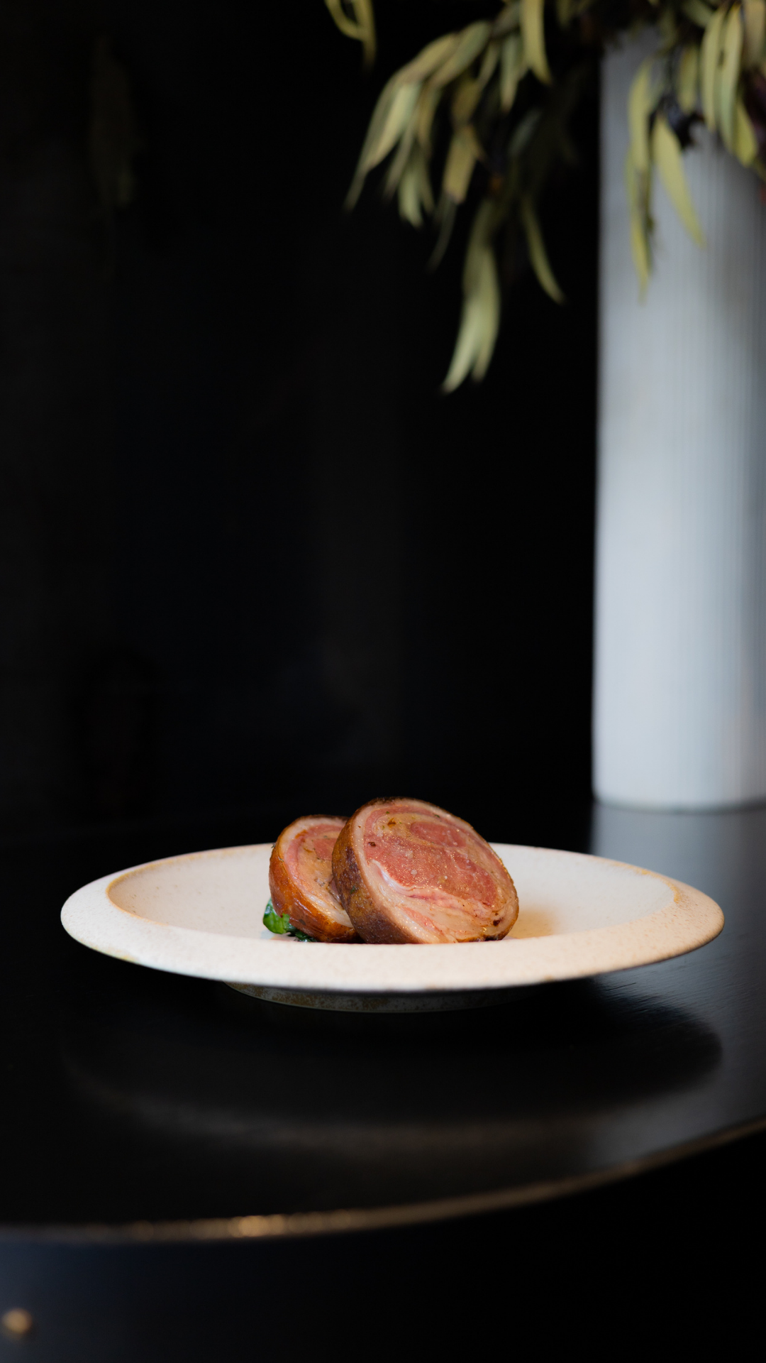 Sliced medium-rare lamb medallions artfully plated on white ceramic dish.