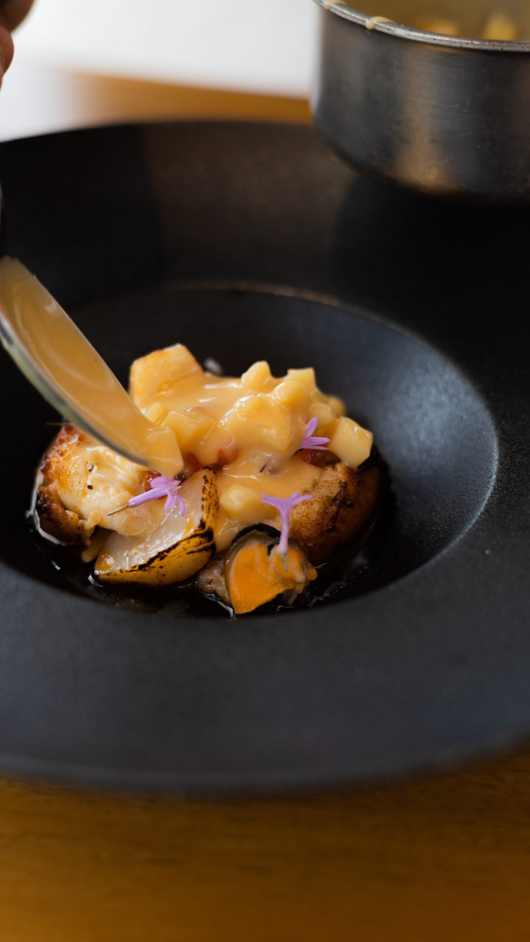Close-up of seafood dish with purple flower garnish in black bowl.