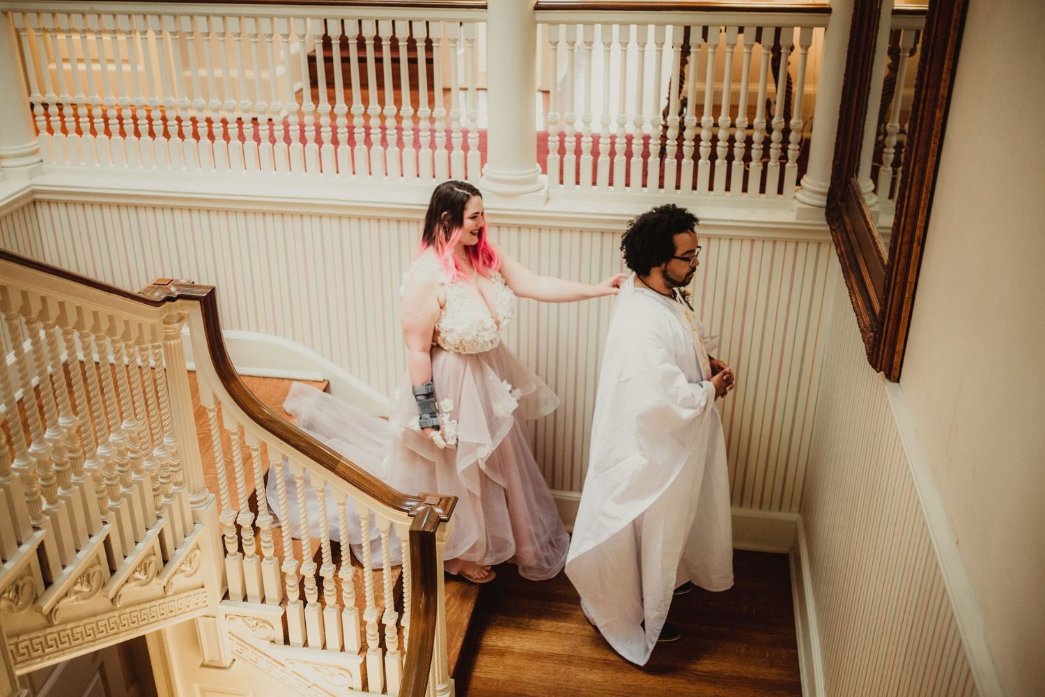 a wedding couple is about to have their first look, she has pink hair and walks downstairs to tap them on their shoulder