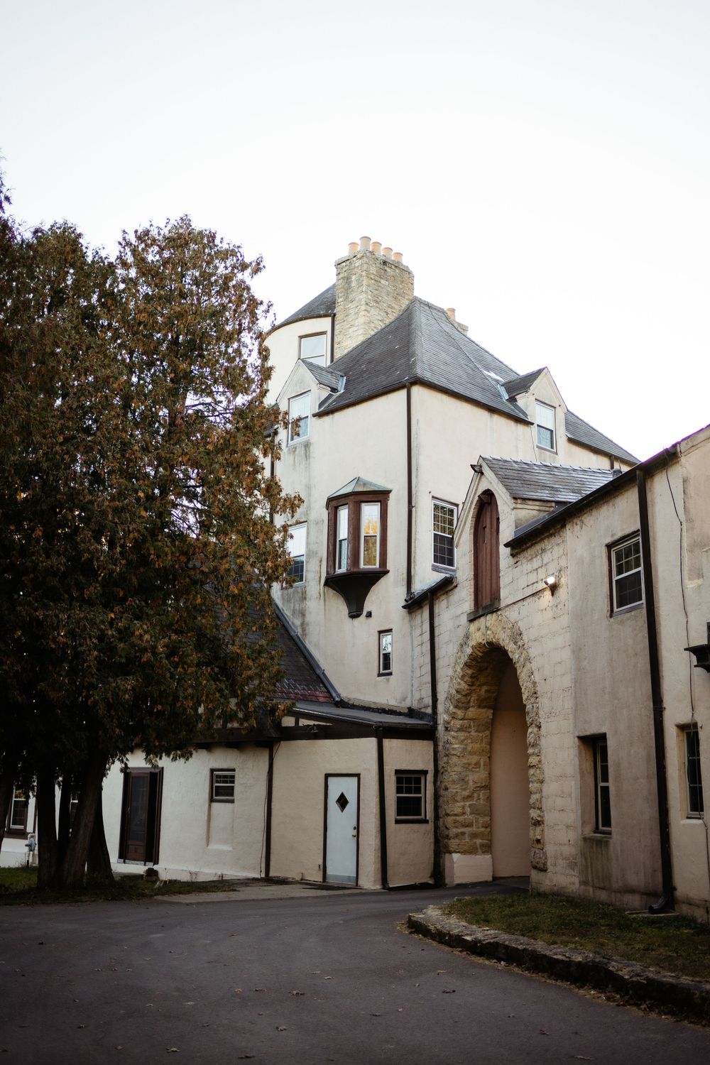 A grand stone building with Tudor-style architecture and arched doorways stands against an overcast sky.