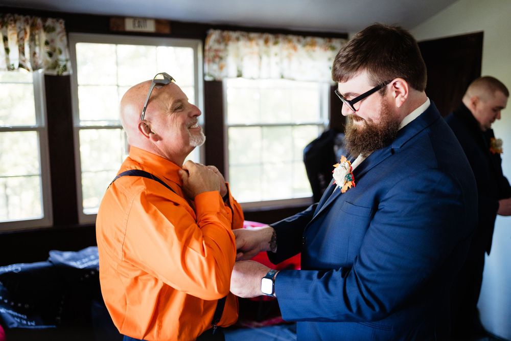 Two people adjusting formal wear and helping with preparations before the ceremony.