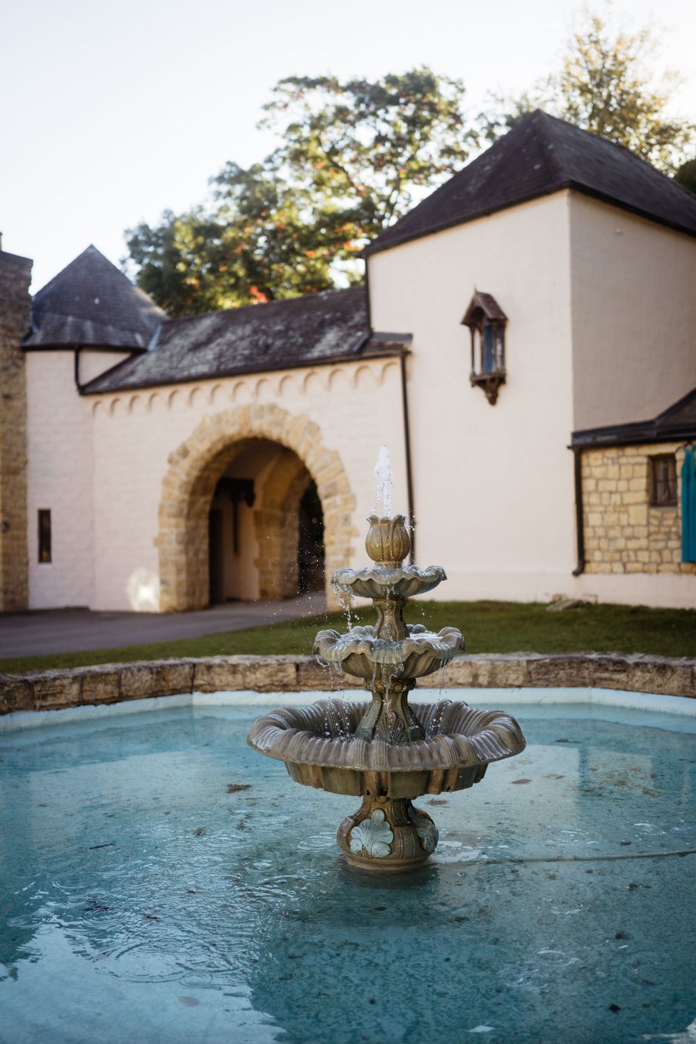 Elegant stone fountain in front of a cream-colored castle-style building.