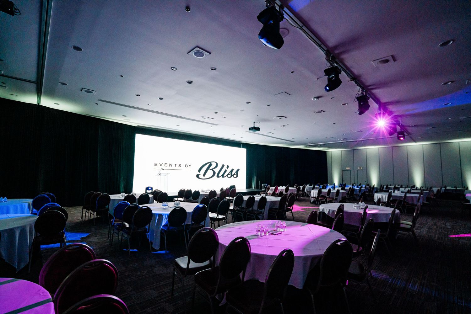An empty event venue with round tables and purple accent lighting.