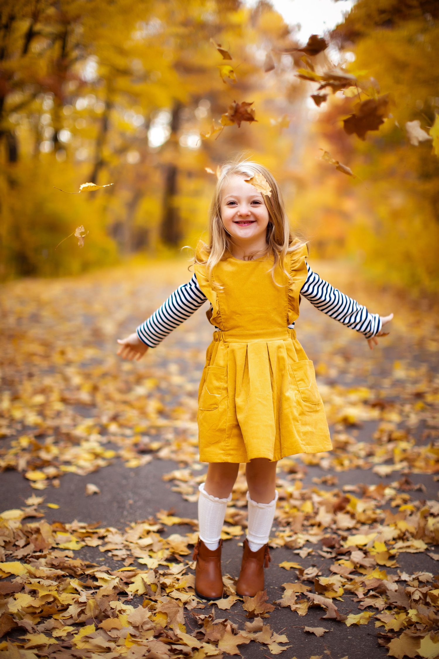 Little girl in a yellow dress plays in the fall leaves during a mini photography session