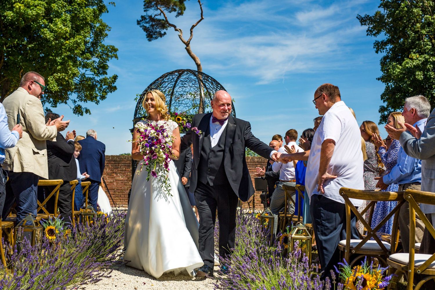 Wedding ceremony taking place in a beautiful garden with guests seated on wooden chairs.