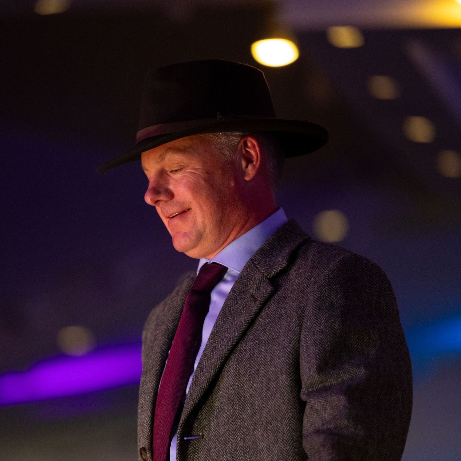 Man in a suit and fedora hat on stage with purple lighting.