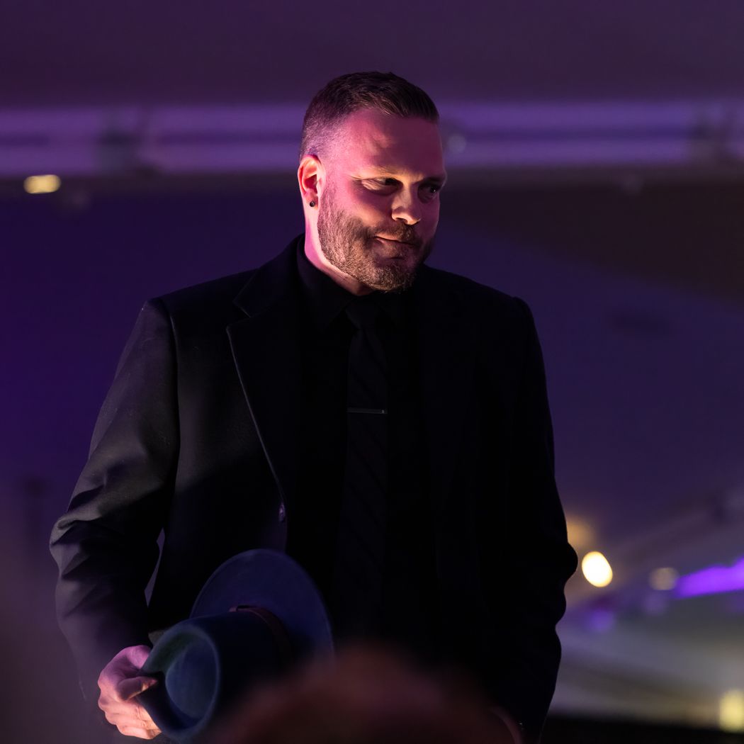 Person on stage wearing black clothing and holding a microphone in dramatic lighting.