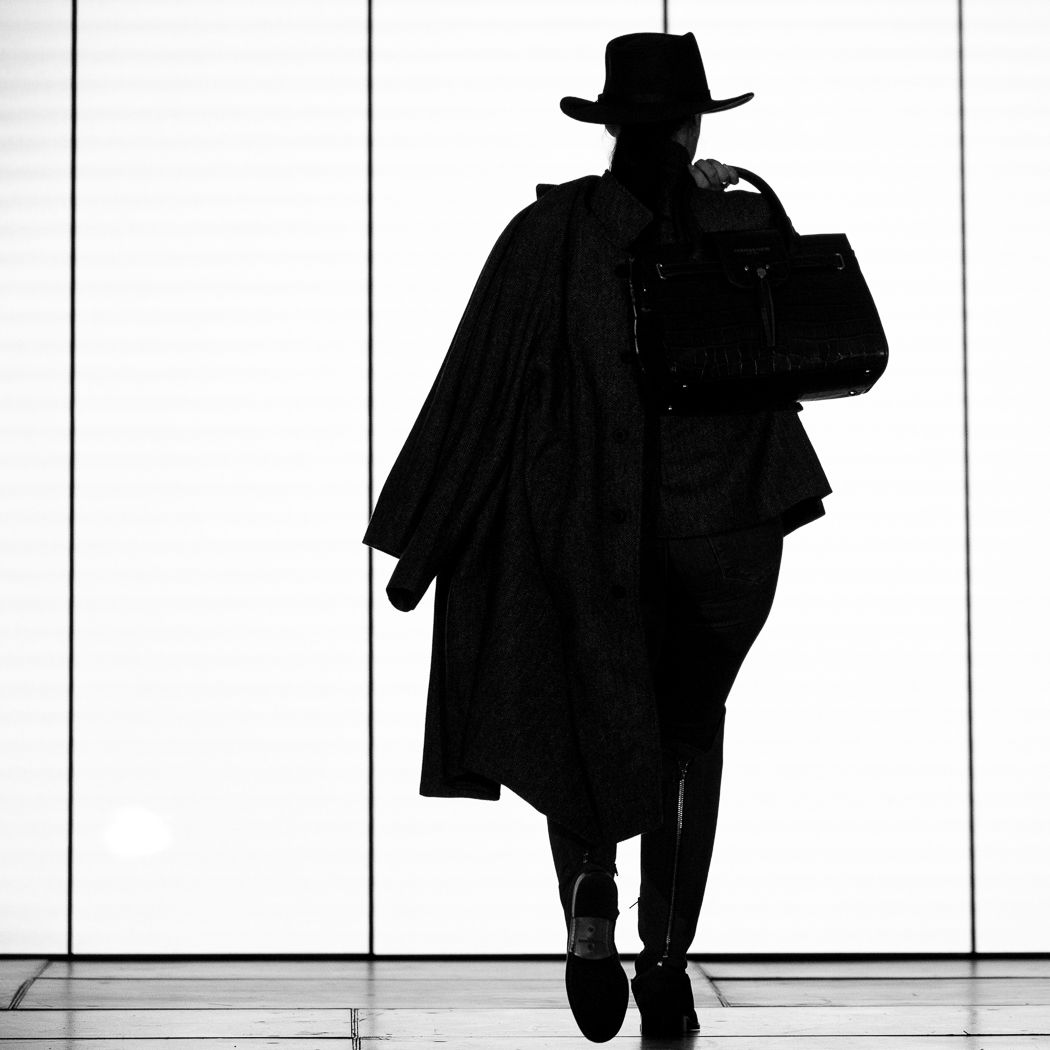 Silhouette of a person in a hat and long coat against a white background.