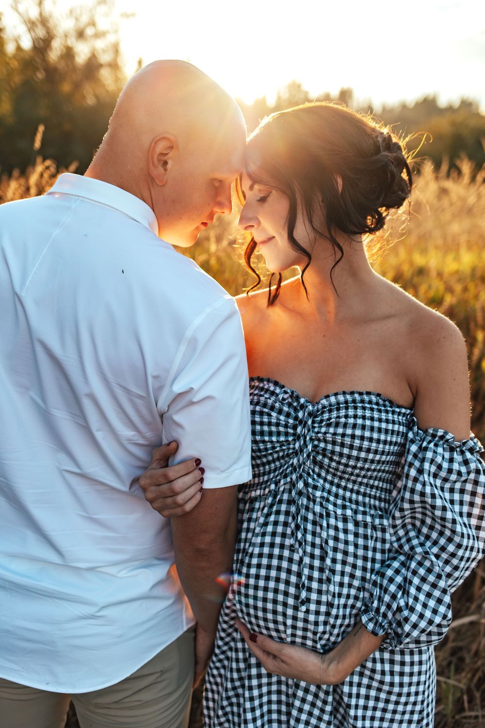 Pregnant woman holding her belly and her husbands arm during golden hour sunny glow