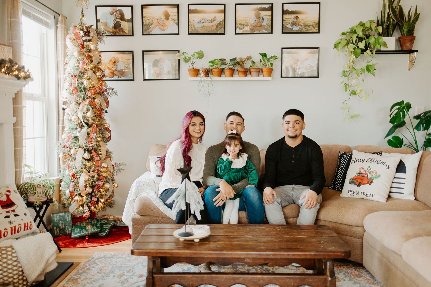 Family of four sitting on a couch in a festive living room decorated with a Christmas tree and framed wall art.