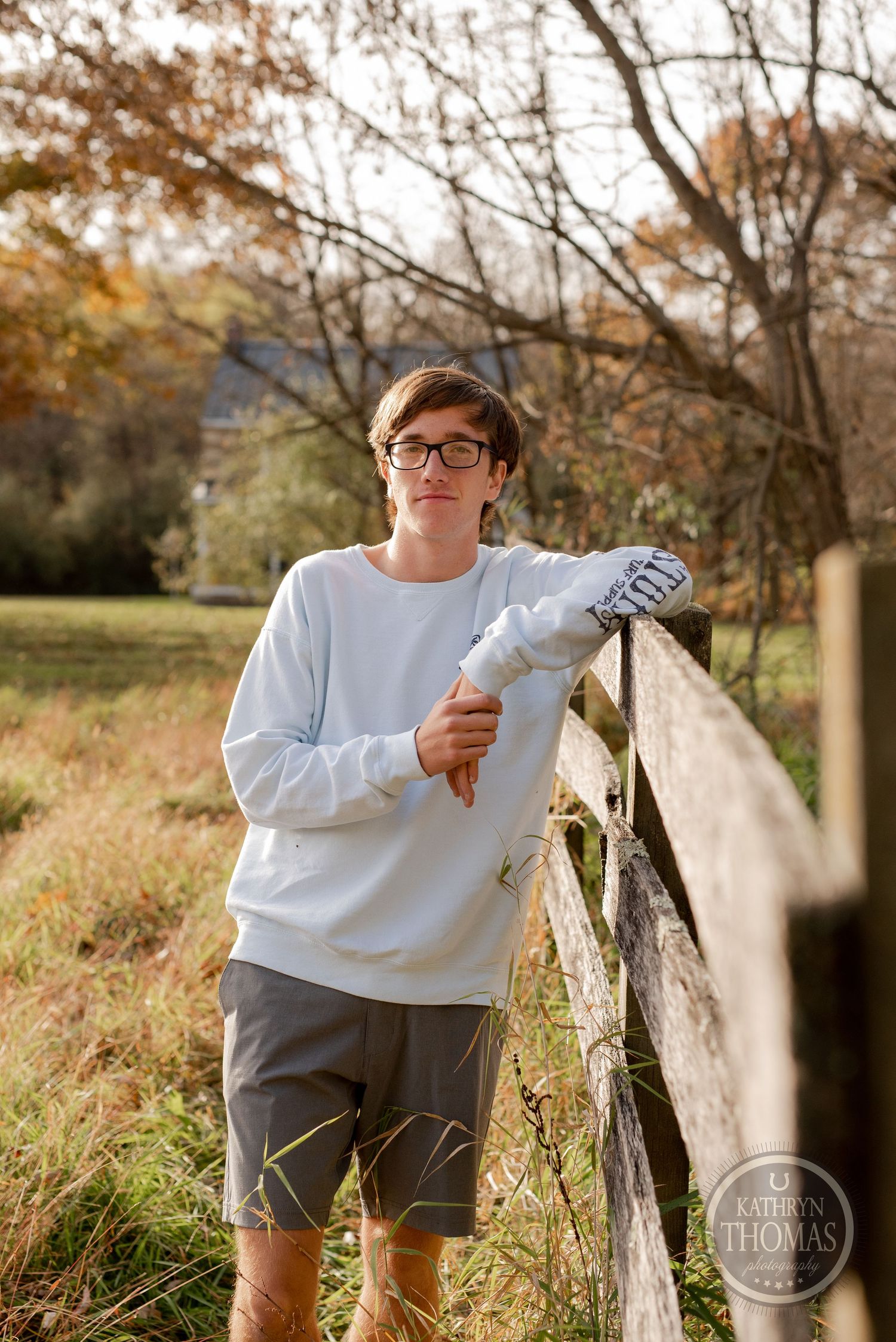 Person in white sweatshirt leans against wooden fence in autumn landscape.