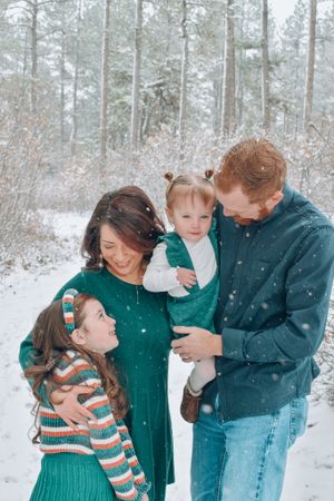 Happy family of four enjoying snowy winter forest during light snowfall.
