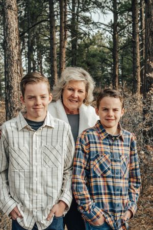 Grandmother smiling with two teenage grandsons in pine forest setting.