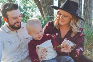 Young couple with toddler son sitting outdoors under shady trees in autumn.