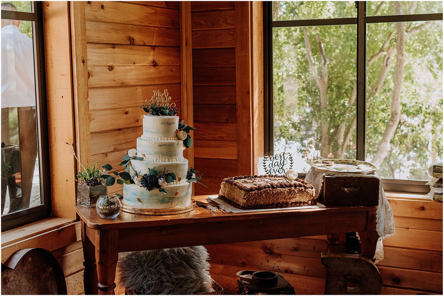 An elegant three-tier wedding cake displayed on a wooden table in a rustic venue with natural lighting.