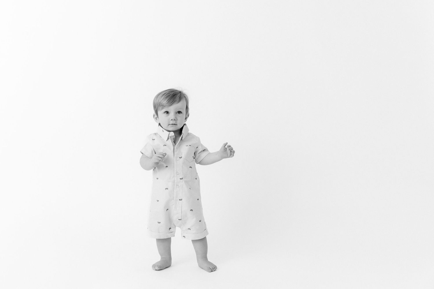 One year old baby in a collared one piece with boats stands ready to take a few steps.