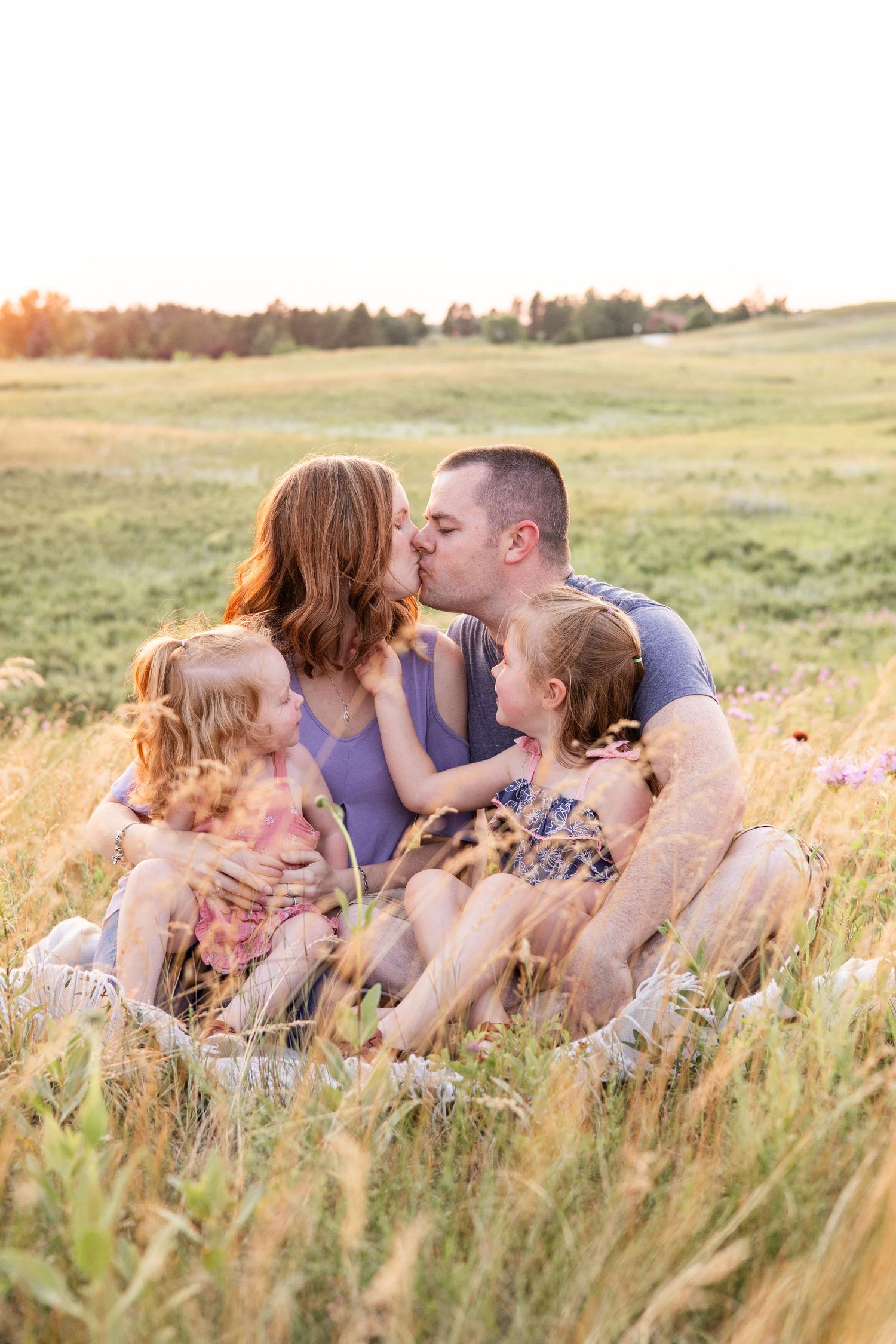 Family sharing intimate moment together in tall grass field at sunset.