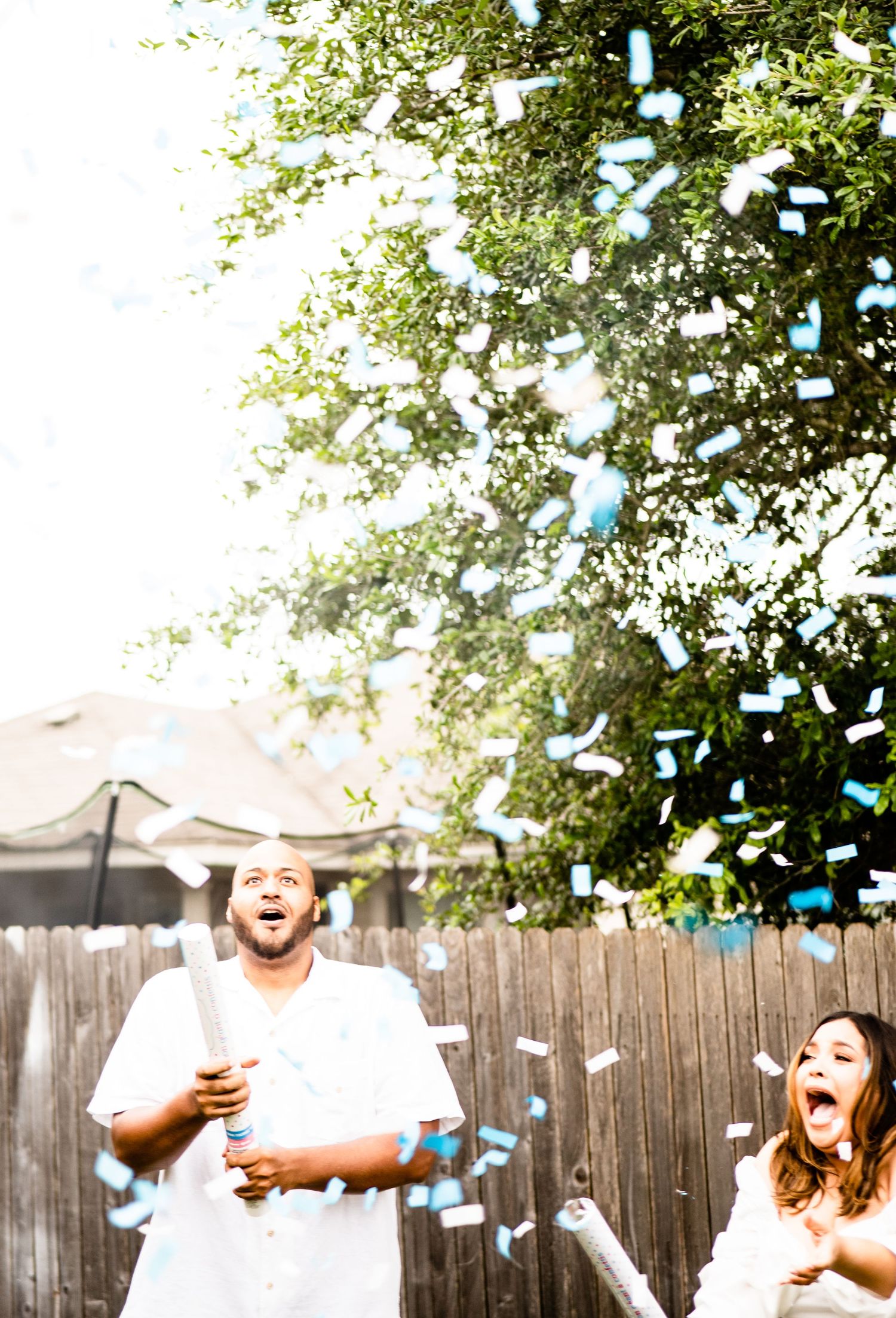Couple captured with the gender reveal outcome of blue confetti exploding in a backyard in Converse, Texas.