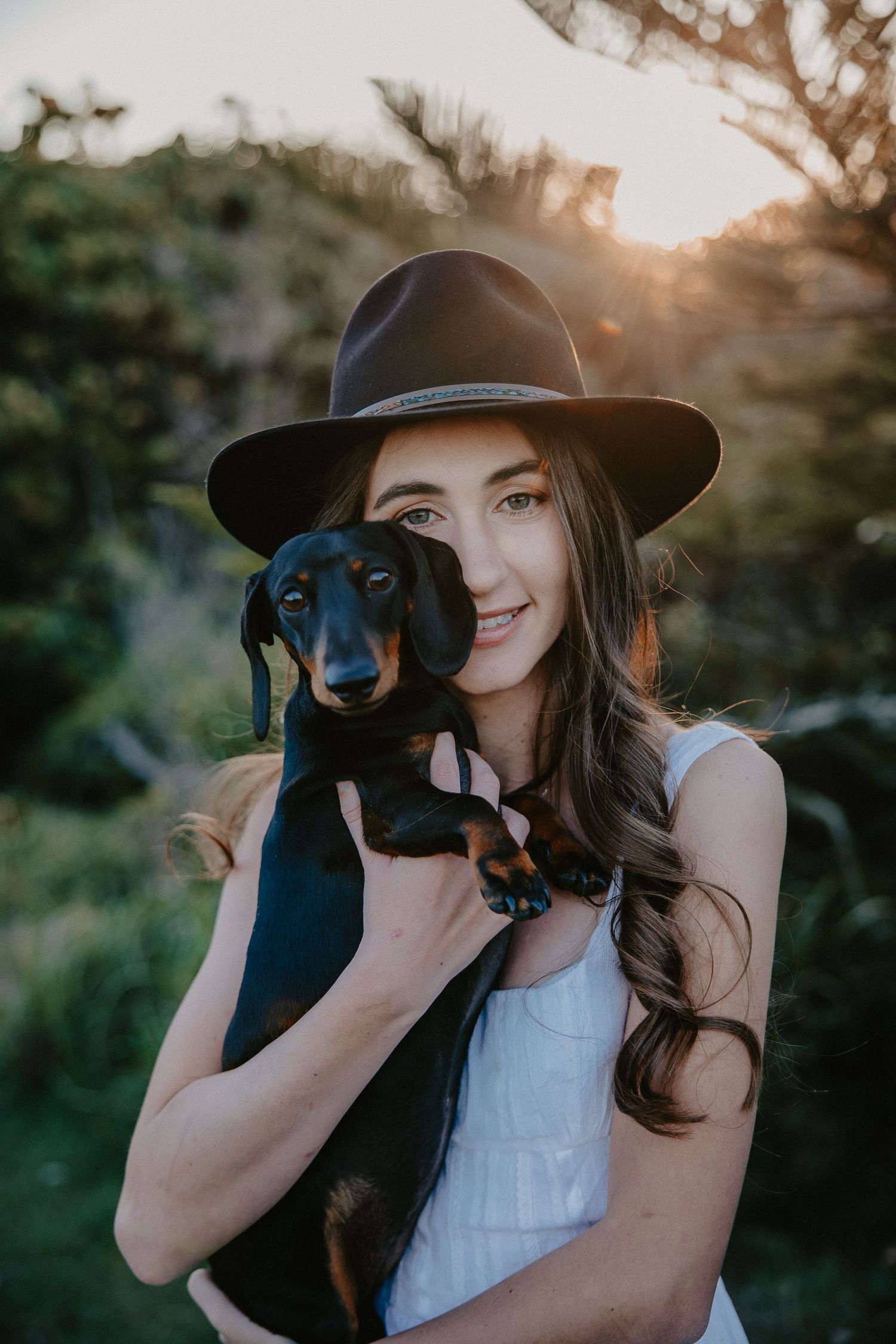 A dachshund puppy being held while wearing a hat in a natural outdoor setting.