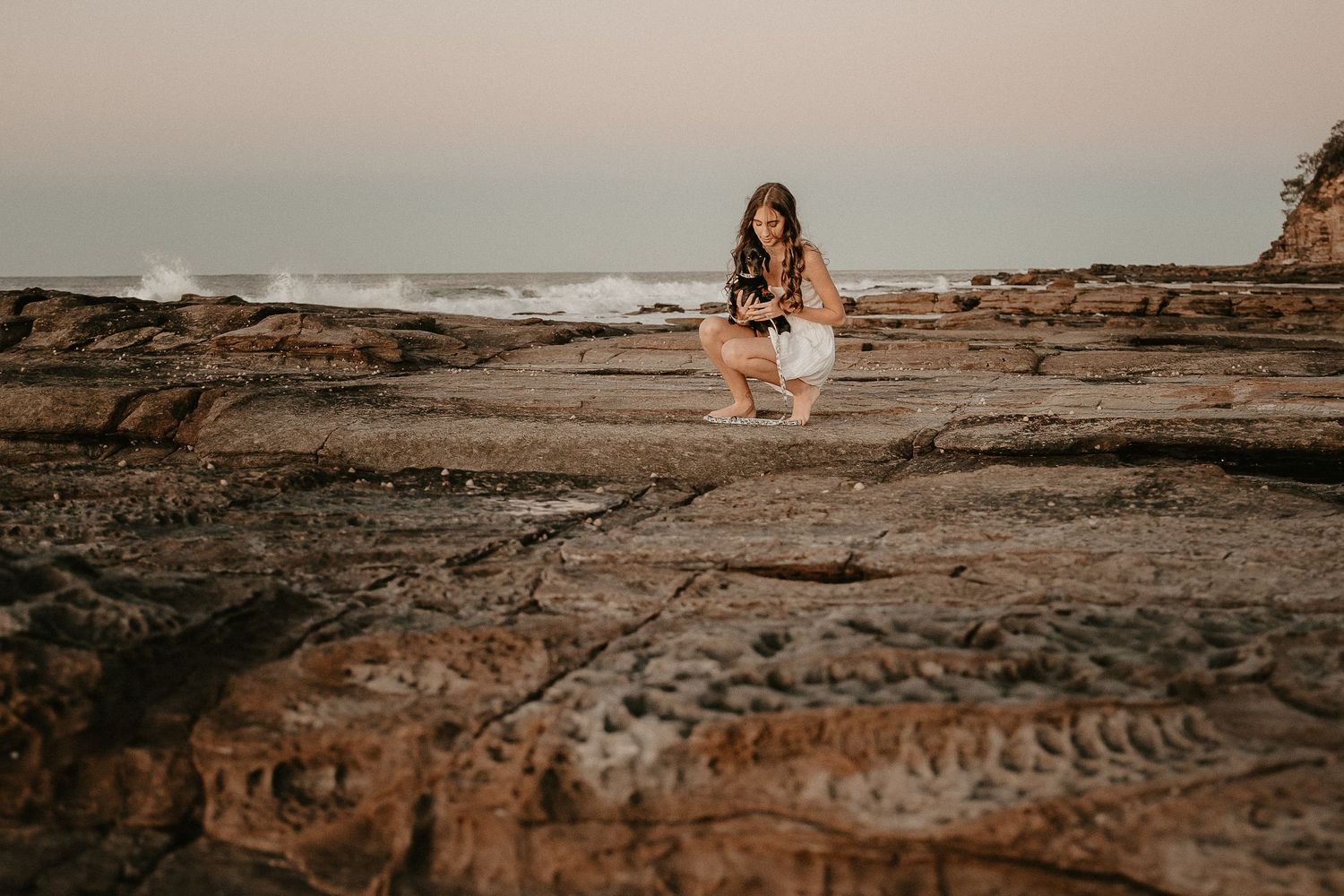 A person sitting on coastal rocks during sunset overlooking the ocean.