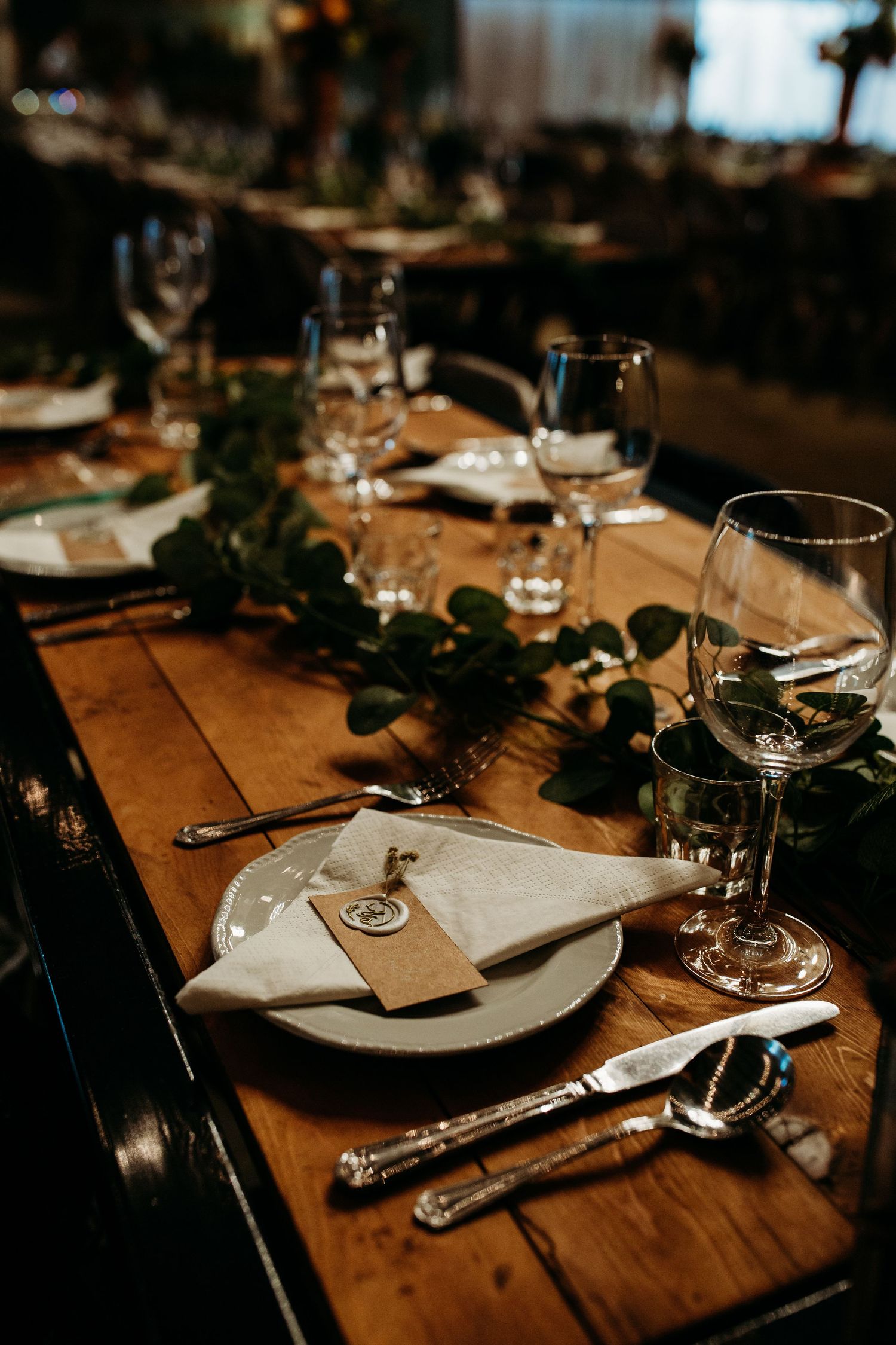 Close-up of elegant place setting with white napkin, wine glasses and greenery on wooden table.