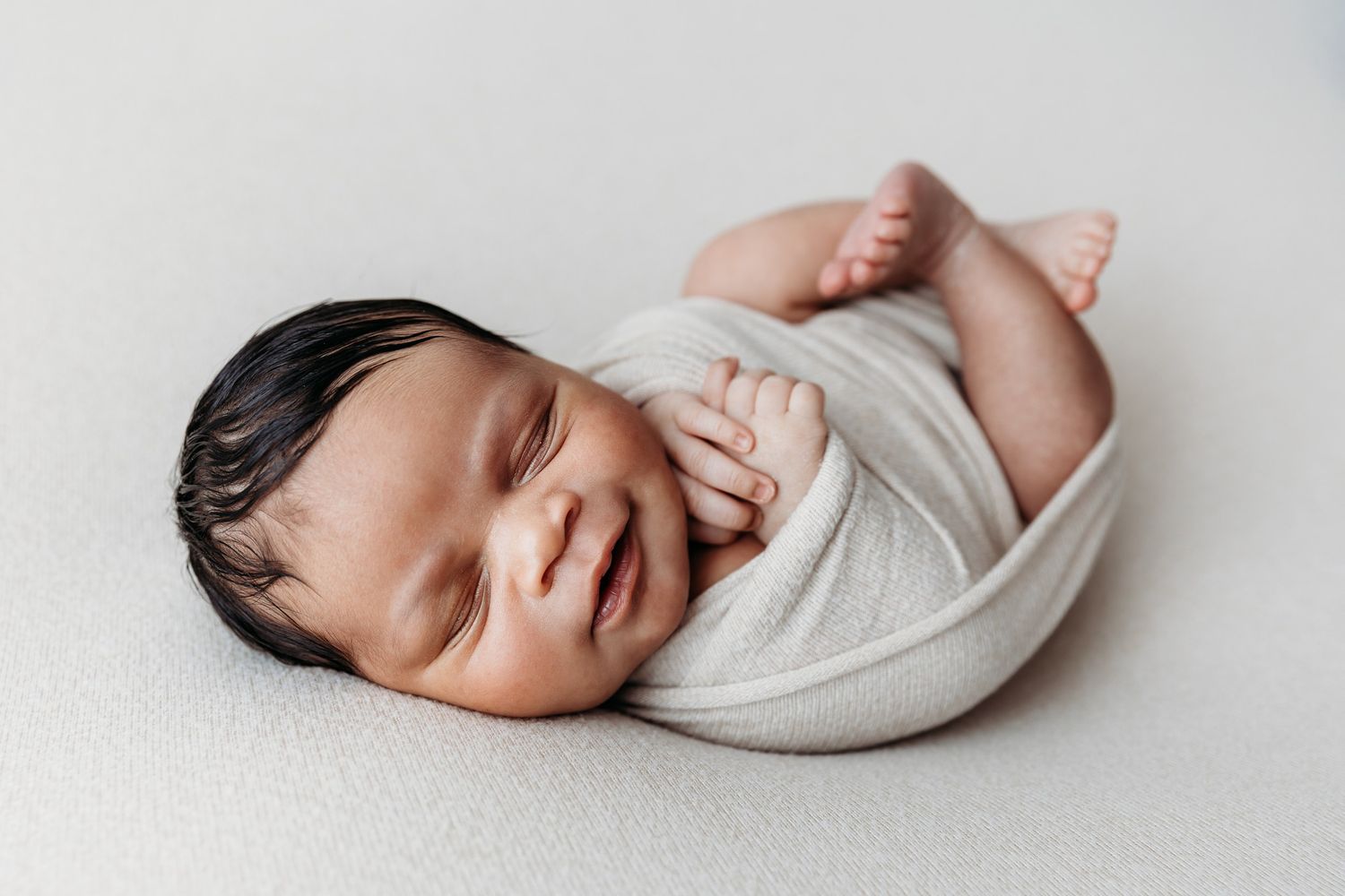 Peaceful newborn baby sleeping in white wrap on light background.