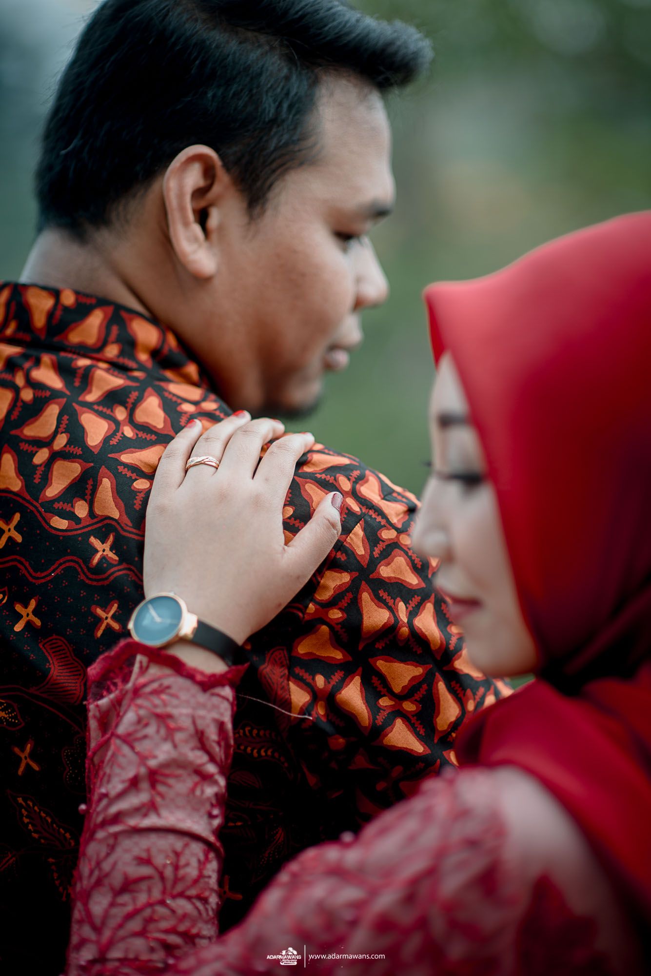 Close-up shot of couple in matching red and brown traditional Indonesian wedding attire.