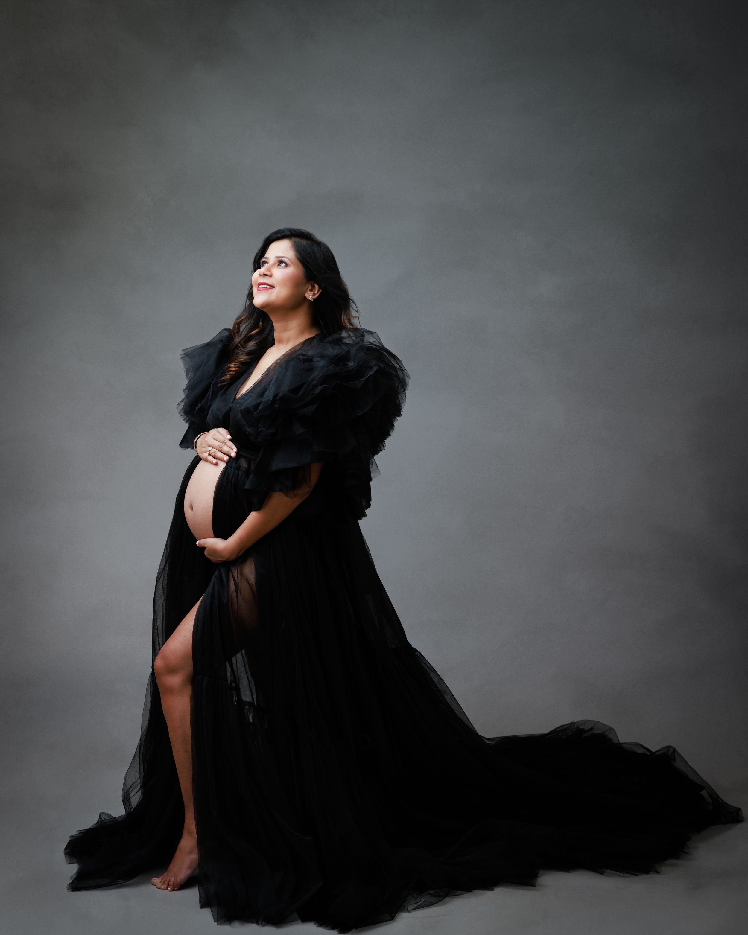 A dramatic maternity photo with a black flowing gown against a grey backdrop.