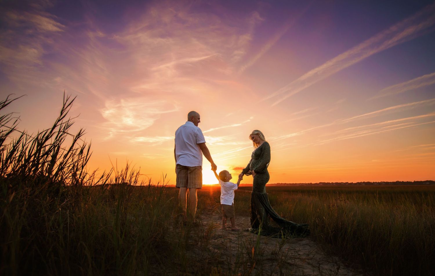Silhouettes of people and their dog standing in a field during a vibrant orange sunset.