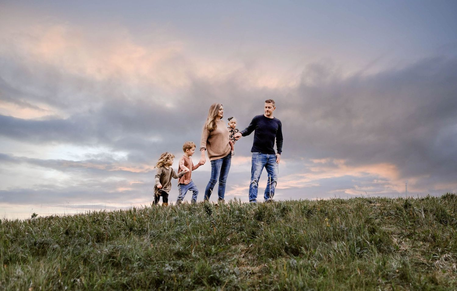 Family walking together on hilltop at sunset with dramatic cloudy sky.