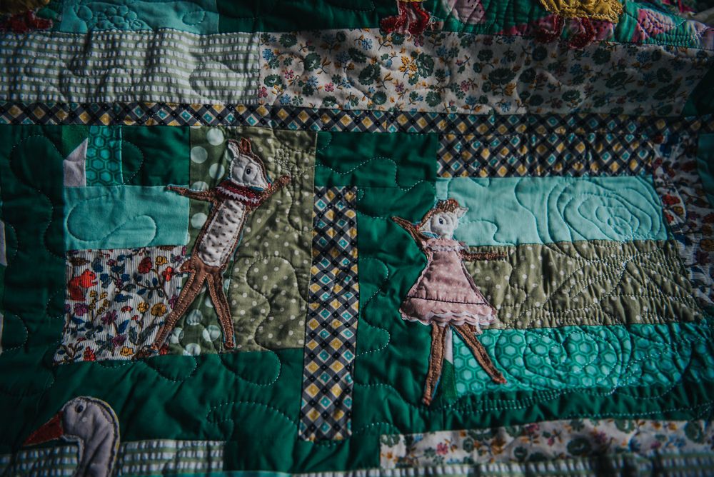 Two deer applique dancing together on a memory quilt made from baby clothes.